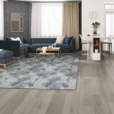 Modern living and dining area with a dark blue sectional sofa, abstract blue and white rug, and a white counter with bar stools, lit by large windows.